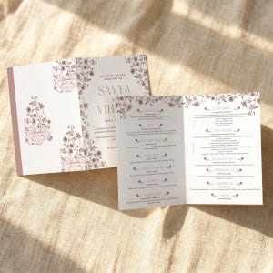 May include: Wedding invitation suite with a floral design in pink and white. The invitation includes the names "Savya" and "Vih", along with event details. The suite features a menu and event details.