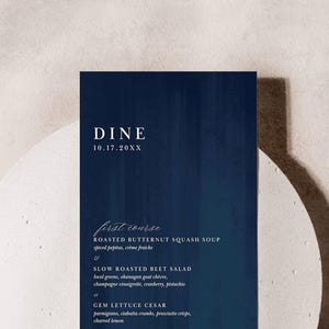 Może przedstawiać: Karta menu weselnego w kolorze granatowym z białym tekstem. Menu zawiera przystawkę z pieczonej zupy z dyni butternut, po której następuje wybór sałatki z pieczonej buraczki lub sałatki Cezar z sałaty gem. Data ślubu jest podana jako 10.17.20XX.