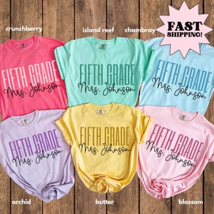 Può includere: Una collezione di sei magliette Fifth Grade colorate. Le magliette sono nei toni del rosa, verde, blu, viola, giallo e rosa. Ogni maglietta ha la scritta "FIFTH GRADE Mrs. Johnson" stampata sul davanti.