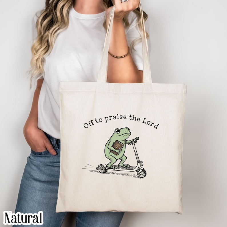 Natural canvas tote bag featuring a cute frog riding a scooter with “Off to praise the Lord” text, Christian faith graphic tote, whimsical religious illustration, reusable shopping bag, boho aesthetic accessory, inspirational Christian gift
