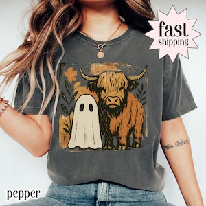 May include: Dark grey t-shirt with a Highland cow and ghost graphic. The cow is brown and tan, the ghost is white. The shirt has the word "pepper" printed at the bottom and a "fast shipping" graphic. A fun, quirky design.
