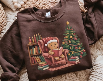 May include: Chocolate-coloured sweatshirt with a gingerbread man reading a book in an armchair, alongside a Christmas tree and bookshelf. The word "chocolate" is printed at the bottom.
