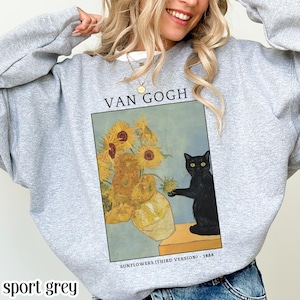 Puede incluir: Sudadera gris deportiva con un estampado de "Girasoles (Tercera versión)" de Van Gogh y un gato negro. La obra de arte incluye un jarrón con girasoles y el texto "VAN GOGH". El texto "SUNFLOWERS (THIRD VERSION) - 1888" está debajo.