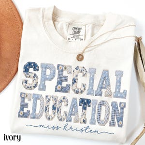Könnte beinhalten: Elfenbeinfarbenes T-Shirt mit den Worten "SPECIAL EDUCATION" in blauen Patchwork-Buchstaben. Das Shirt hat auch die Worte "miss kristen" in Schreibschrift und eine goldene Halskette. Das Shirt ist von der Marke Comfort Colors.