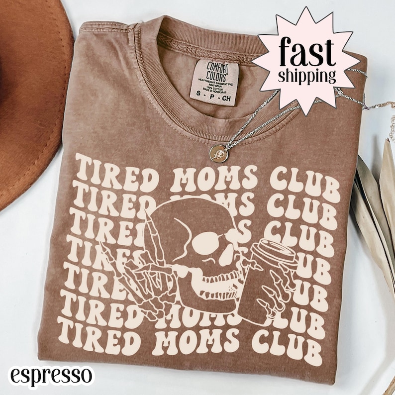 Espresso brown Comfort Colors t-shirt featuring a bold “Tired Moms Club” graphic with repeating retro text and a skull holding a coffee mug, a funny mom graphic tee perfect for tired moms, coffee lovers, motherhood humor, and everyday casual wear