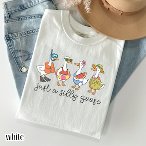 White “just a silly goose” graphic t-shirt featuring cute geese in summer outfits, funny animal shirt, playful humor tee, women’s casual graphic top, trendy aesthetic apparel, cute gift idea for goose lovers