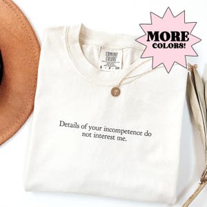 Cream Comfort Colors t-shirt featuring minimalist black text reading details of your incompetence do not interest me centered on the chest. Soft-washed cotton short sleeve graphic tee with simple typography design, neutral aesthetic, and subtle sarcastic statement style