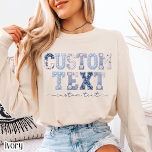 May include: An ivory long-sleeve sweatshirt featuring the words CUSTOM TEXT in large, block-style letters filled with various blue and white floral, gingham, and polka dot patterns, with the words custom text written in a cursive blue script below.