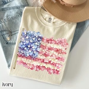 Ivory patriotic floral graphic t-shirt featuring American flag made of pink and blue hydrangea flowers, Fourth of July shirt, feminine USA pride tee, Independence Day apparel, cottagecore patriotic top, women’s summer graphic t-shirt
