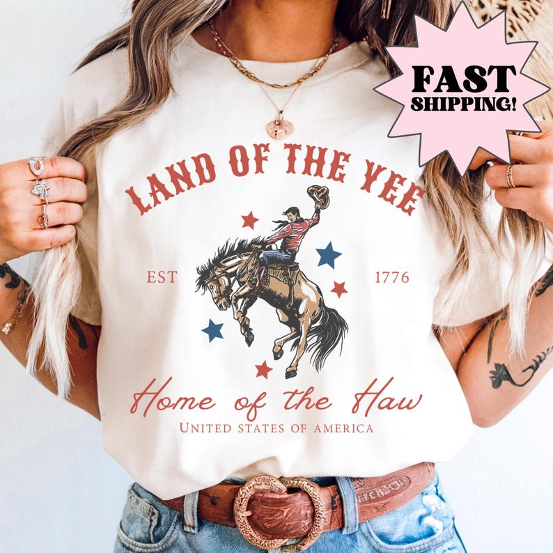 Cream graphic shirt featuring a western-style patriotic illustration of a cowboy riding a bucking horse with red and blue stars and text reading “Land of the Free” and “Home of the Brave.” Patriotic western graphic tee designed as Americana apparel, rodeo-inspired shirt, and USA pride statement tee