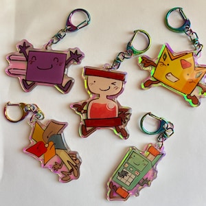 May include: Five acrylic keychains with iridescent edges and rainbow-colored metal clasps. The designs feature cartoon characters: a purple square, a red hourglass shape, a yellow crown, a multi-colored geometric shape, and a green calculator.