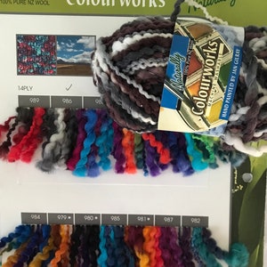 May include: A skein of hand-painted chunky yarn in shades of gray, white, and brown. The yarn is labeled "Colourworks Naturally" and is 100% pure New Zealand wool. The label also states that the yarn is machine washable. A color chart shows a variety of colors, including red, orange, yellow, green, blue, purple, and black. The yarn is 14 ply and comes in a ball size of 50 grams.