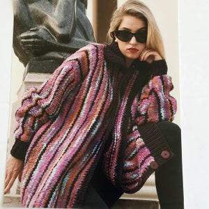 May include: A long, striped cardigan with a zipper closure. The cardigan is made of a soft, knitted fabric and features a variety of colors, including pink, purple, blue, and brown. The cardigan is worn by a person with blonde hair and sunglasses.