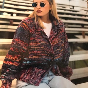 May include: A woman wearing a multi-colored striped cardigan with a white shirt underneath. She is wearing blue jeans and round sunglasses.