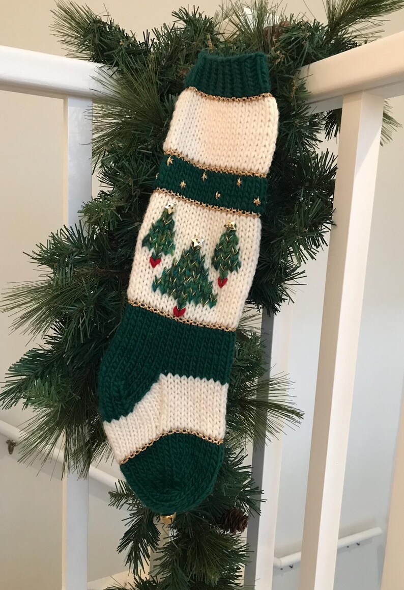 以下が含まれることがあります： 緑と白のニットのクリスマスストッキングで、金と赤のアクセントがついたクリスマスツリーが3本デザインされています。