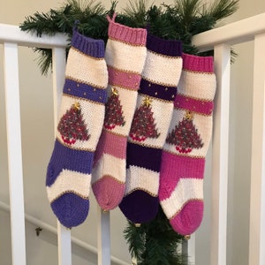 May include: Four knitted Christmas stockings with a white background and colorful stripes. Each stocking features a gold beaded trim and a knitted Christmas tree design with gold beads.