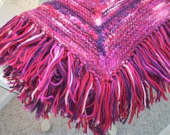 May include: A woven throw blanket with a fringe border in shades of pink, purple, and white.