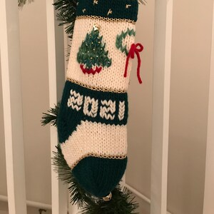 以下が含まれることがあります： 緑と白のニット製のクリスマスストッキング。緑のクリスマスツリーのデザインと、前面に刺繍された2021年が特徴です。