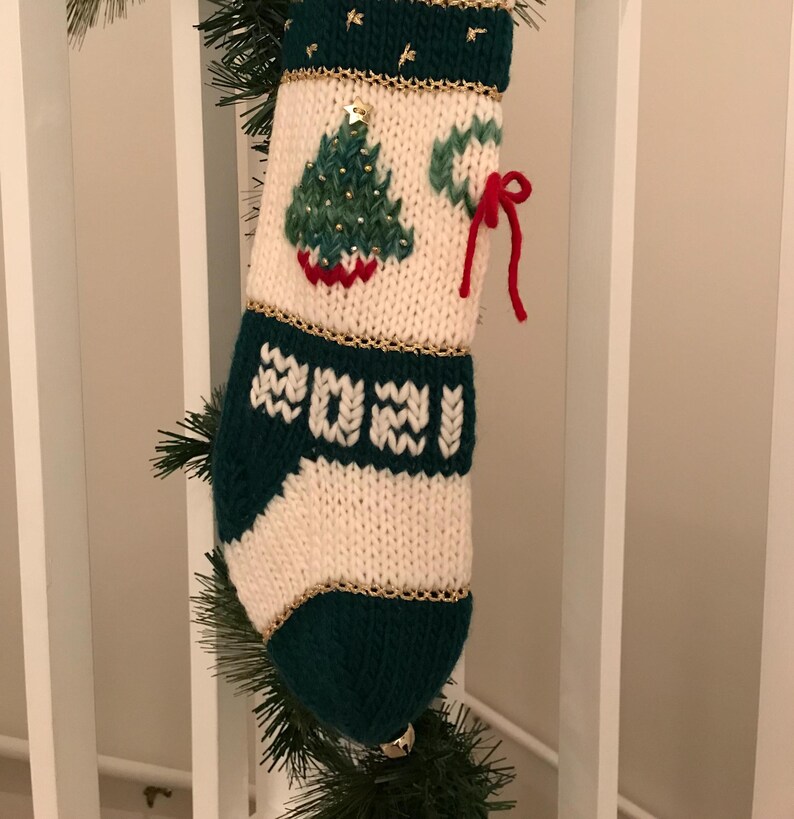 以下が含まれることがあります： 緑と白のニット製のクリスマスストッキング。緑のクリスマスツリーのデザインと、前面に刺繍された2021年が特徴です。