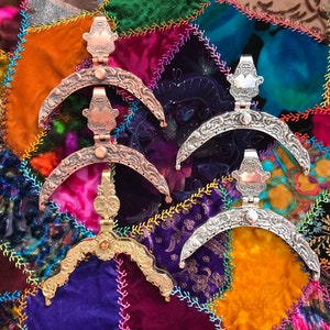 May include: Five decorative metal purse frames in copper, silver, and gold tones. The frames have ornate, curved designs with hinged closures. The background is a patchwork of colorful velvet fabrics.