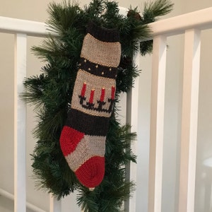 May include: A knitted Christmas stocking with a red, black, and white design. The stocking features a pattern of candles and gold stars.