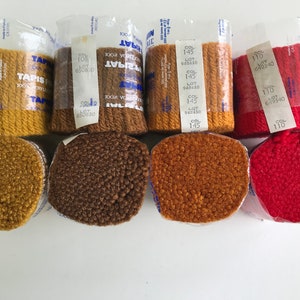 May include: Six spools of yarn in various colors, including brown, orange, and red. Each spool is labeled with a color number and lot number. The yarn is packaged in clear plastic.