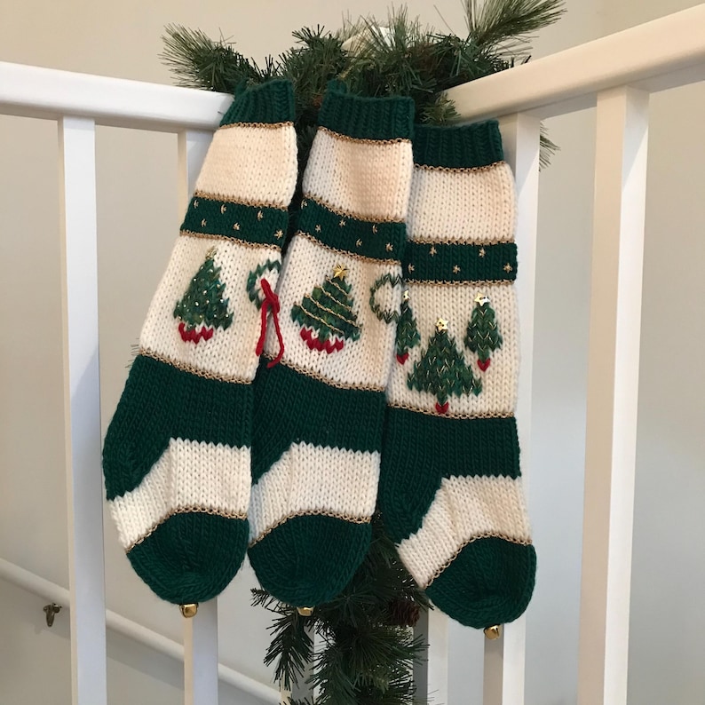 以下が含まれることがあります： 緑と白のストライプのクリスマスストッキングが3つ。刺繍されたクリスマスツリーと金色のトリムが施されています。