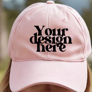 May include: A pink baseball cap with a black text overlay that says "Your design here".