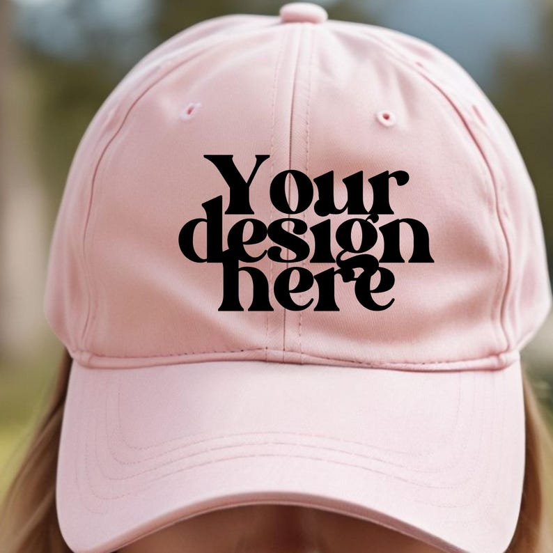 May include: A pink baseball cap with a black text overlay that says "Your design here".