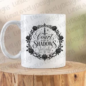 May include: White ceramic mug featuring the text "Court of Shadows" in a gothic font, surrounded by a black floral wreath with roses and thorns. A sword and two crowns are also featured in the design.