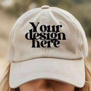 May include: A beige baseball cap with a black embroidered design that says "Your design here".