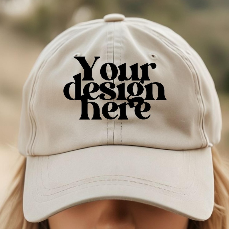 May include: A beige baseball cap with a black embroidered design that says "Your design here".