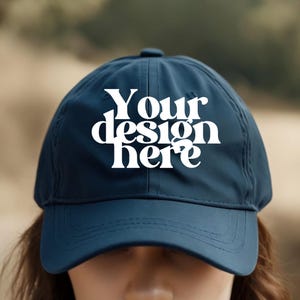 May include: A navy blue baseball cap with a white embroidered design that says "Your design here".