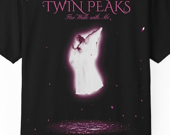May include: A black short-sleeve t-shirt featuring a graphic print with the text TWIN PEAKS Fire Walk with Me. The design displays a glowing white figure against a dark background with pink light accents and small floating particles.