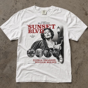 May include: A white short-sleeve t-shirt featuring a black and white graphic print of the film Sunset Blvd. The design includes the movie title in red text, a portrait of Gloria Swanson, a street lamp, and four circular scenes from the movie.