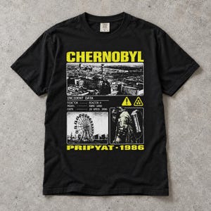 Könnte beinhalten: Ein schwarzes Kurzarm-T-Shirt mit einem gelb-weißen Grafikdruck. Das Design zeigt den Text CHERNOBYL und PRIPYAT-1986, ein schwarz-weißes Bild eines Kraftwerks, ein Riesenrad sowie eine Person, die eine Gasmaske und entsprechende Ausrüstung trägt.