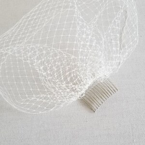 May include: White bridal veil with a comb attached. The veil is made of a fine, delicate netting.