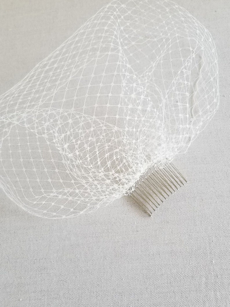 May include: White bridal veil with a comb attached. The veil is made of a fine, delicate netting.