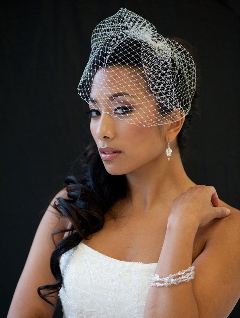May include: A bride wearing a white wedding dress with a veil and a crystal bracelet. Her hair is styled in a side parting with loose curls.