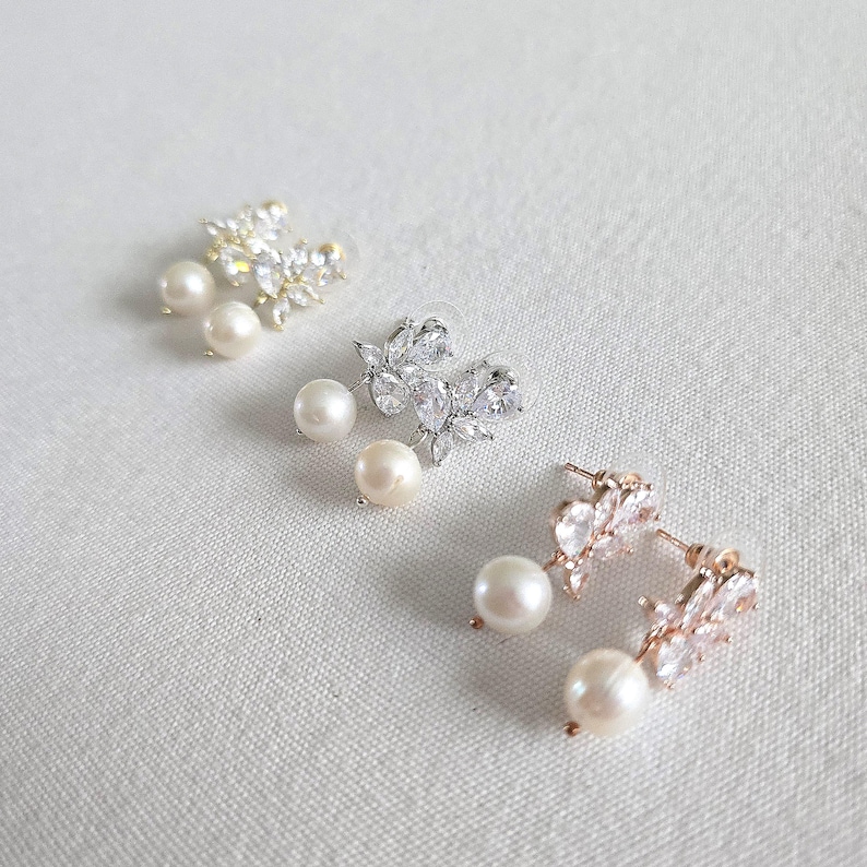 May include: Three pairs of elegant stud earrings. Each earring features a cluster of clear crystals and a dangling pearl. The earrings are in gold, silver, and rose gold tones, set against a white background.