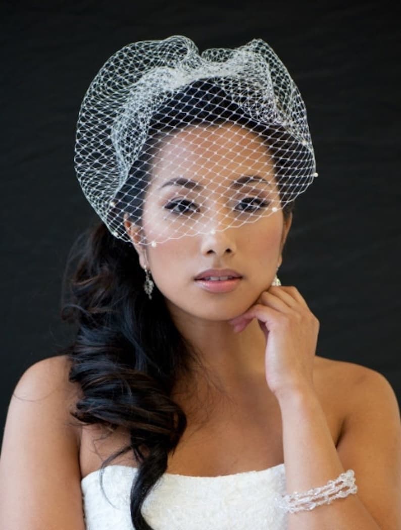 May include: A bride with dark hair wearing a white veil with a pearl trim and a white strapless dress. She is wearing a crystal bracelet on her wrist.