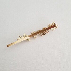 The hair clip features a long, flat base with a series of small, cubic zirconia embellishments and freshwater pearl accents. The clip is designed to secure hair in place.