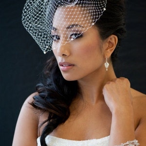 May include: A bride wearing a white wedding dress with a veil and a crystal bracelet. Her hair is styled in a side ponytail and she is wearing diamond earrings.