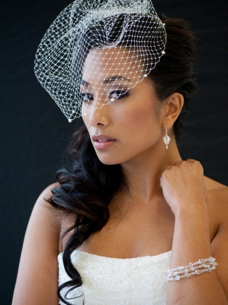 May include: A bride wearing a white wedding dress with a veil and a crystal bracelet. Her hair is styled in a side ponytail and she is wearing diamond earrings.