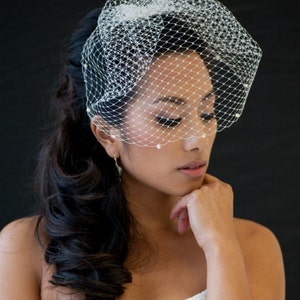 May include: A bride wearing a white wedding dress with a white veil and a beaded bracelet. Her hair is styled in a long, flowing ponytail.