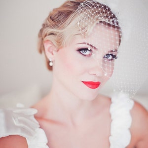 May include: A bride wearing a white wedding dress with a veil and red lipstick. The bride has her hair styled in a vintage updo.