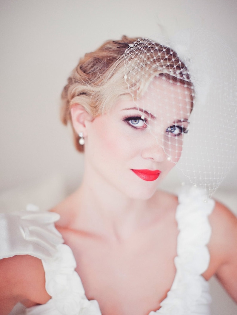 May include: A bride wearing a white wedding dress with a veil and red lipstick. The bride has her hair styled in a vintage updo.