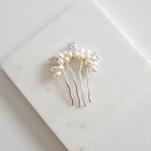 Puede incluir: Un peine de pelo plateado con una fila de perlas blancas y diamantes de imitaci&oacute;n transparentes.