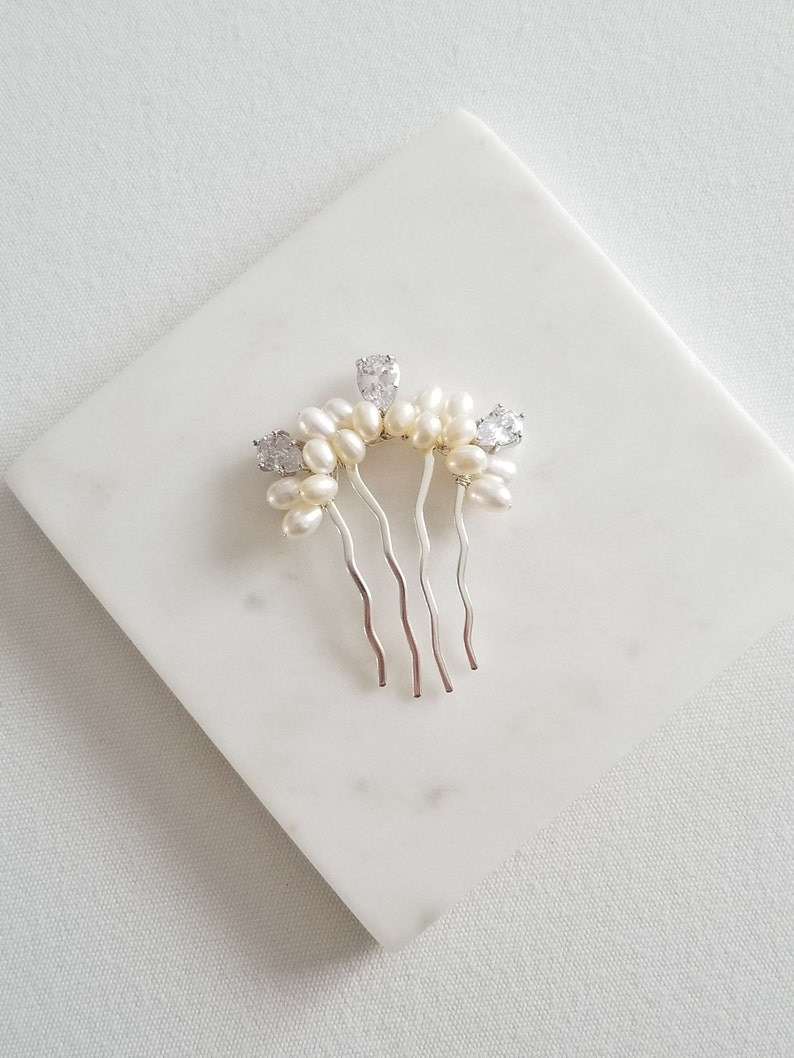 Puede incluir: Un peine de pelo plateado con una fila de perlas blancas y diamantes de imitaci&oacute;n transparentes.
