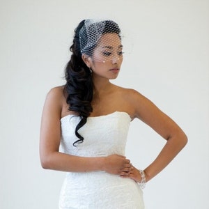 May include: A bride wearing a white strapless wedding dress with a veil and a delicate bracelet. Her hair is styled in a long, flowing ponytail.